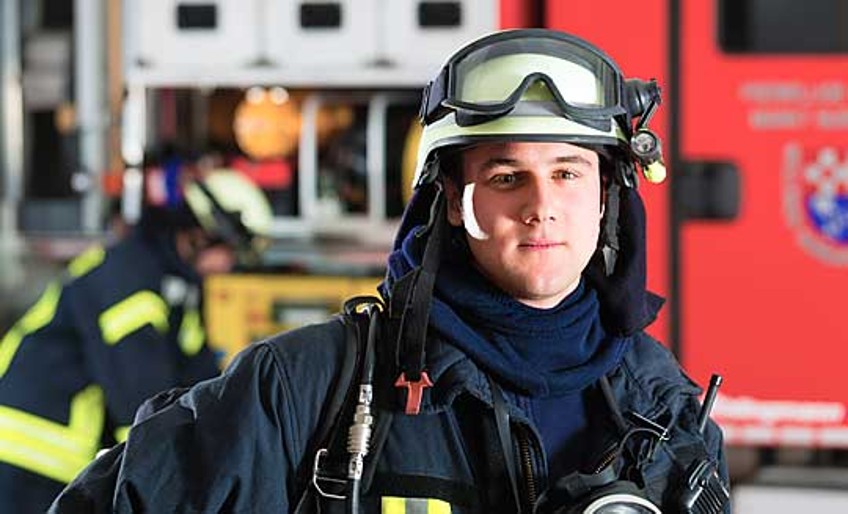 DEVK-Quereinsteiger - Feuerwehrmann vor Einsatzwagen