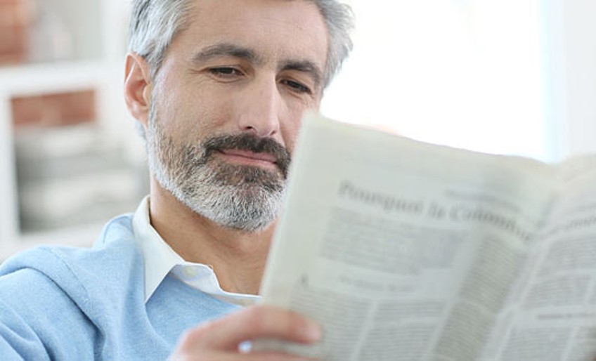 Schlagzeilen - Mann liest Zeitung auf Sofa